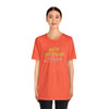 Female model wearing orange cotton shirt by Top Knot Goods that says Meet Me Under The Bleachers, Lets Play Sports.