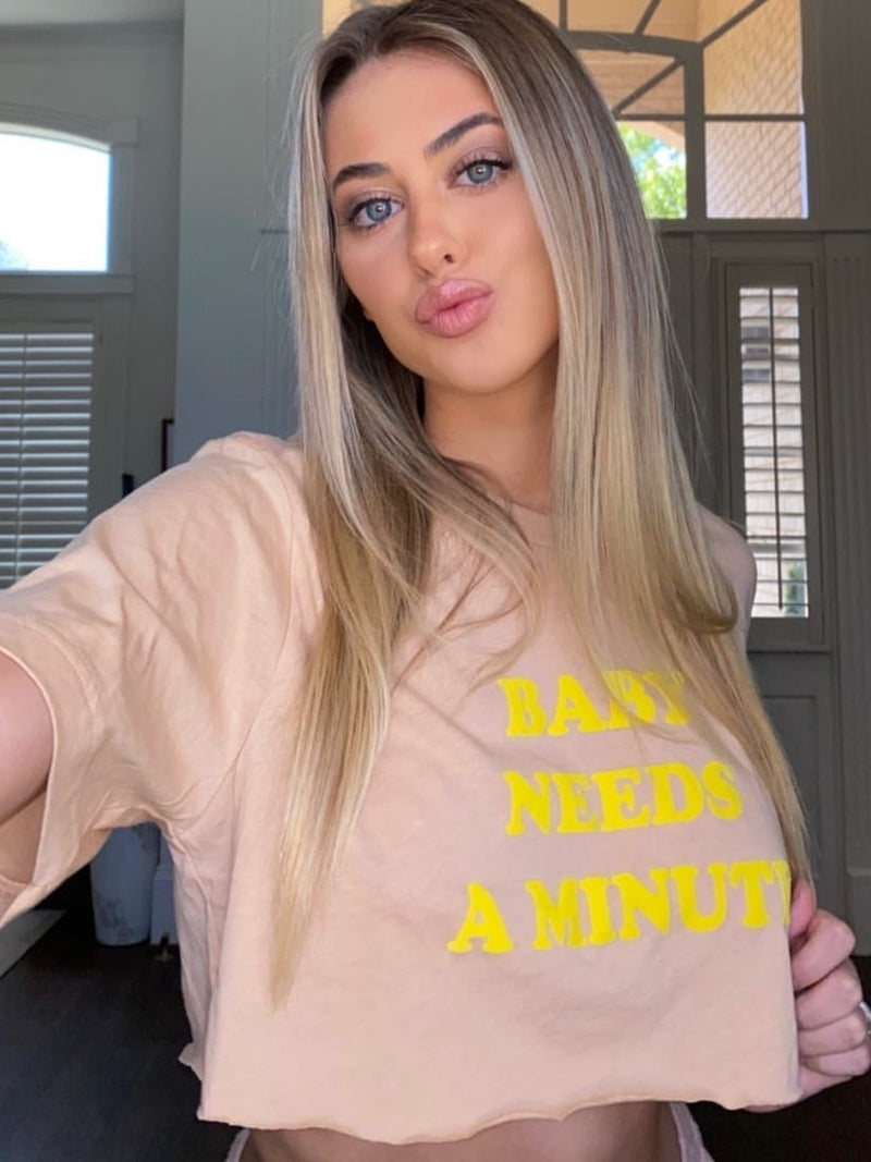 Top Knot Goods sand colored T-Shirt that says "Baby Needs a Minute."