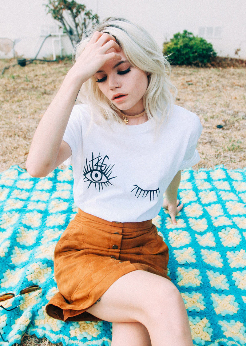 Female model wearing Top Knot Goods white cotton logo t-shirt with winking eyes with brand logo in the eyelashes.