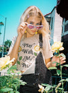 Model wearing sunglasses and tan shirt with Play With My Petals with two flowers on the front.