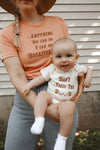 Mother holding baby that is wearing a funny baby onesie that says Baby Needs the Boob