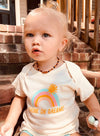 Baby girl wearing cute baby tee that says Drunk on Dreams with a colorful rainbow